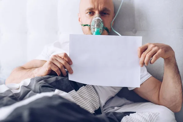 Paciente enfermo por Coronavirus respirando a través de máscara de oxígeno y sosteniendo tarjeta vacía — Foto de Stock