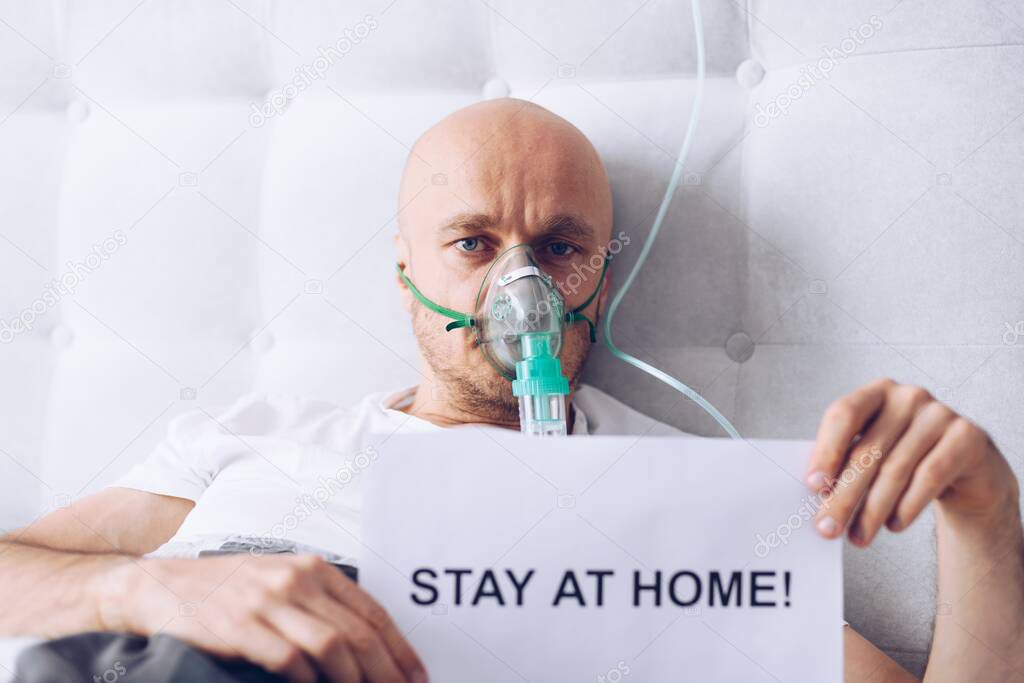 Sick man breathing through oxygen mask and holding card with message stay at home