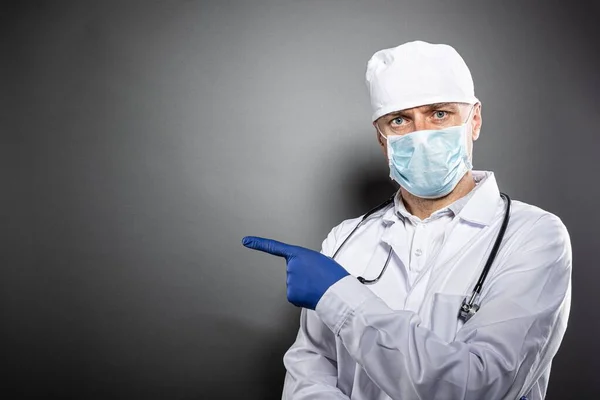 Doctor in white uniform and protective medial mask pointing left — Stock Photo, Image