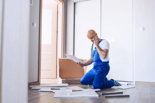 Nervous man assembling cabinet and reading manual