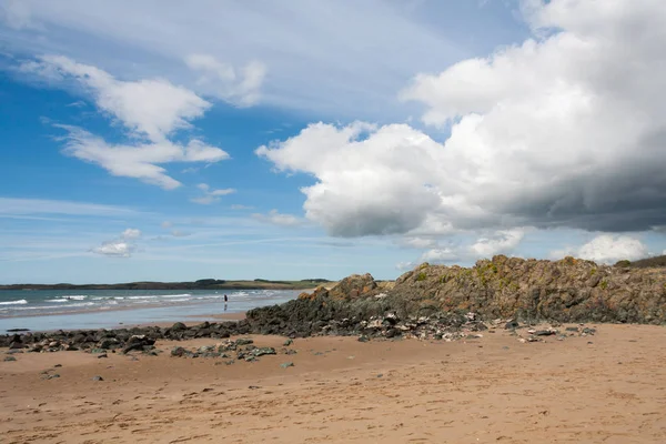 Rocha vulcânica, céu azul e nuvens na praia de Newborough, Anglesey — Fotografia de Stock