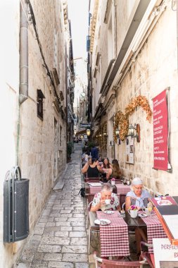 Dubrovnik, Hırvatistan - 24 Eylül 2017: İnsanlar dar sokaktaki bir restoranda yemek yiyor. Şehir aşırı kalabalık nedeniyle yolcu gemisi sayısını sınırlandırmayı düşünüyor..