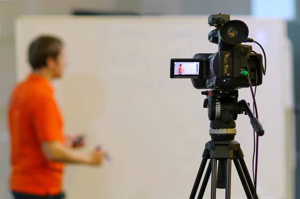 Behind-the-scenes shooting of a video product or lecture. Shooting a person next to a white Board with a video camera