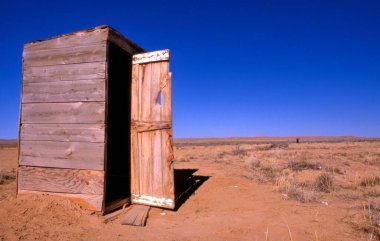 Kırsal alanda küçük ahşap tuvalet, açık mavi gökyüzüne karşı.