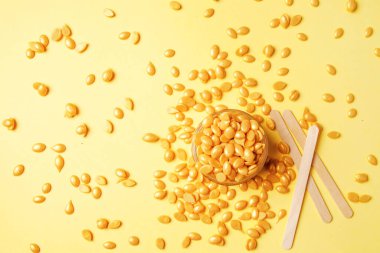 Altın renkli balmumu, tüy dökücü spatula, sıcak balmumu tipi, yüz ve vücut için, sarı arka planda altın tanecikler.