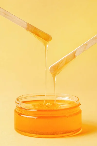 Honey in a jar on a yellow background flows, spatulas for depilation, natural wax for depilation