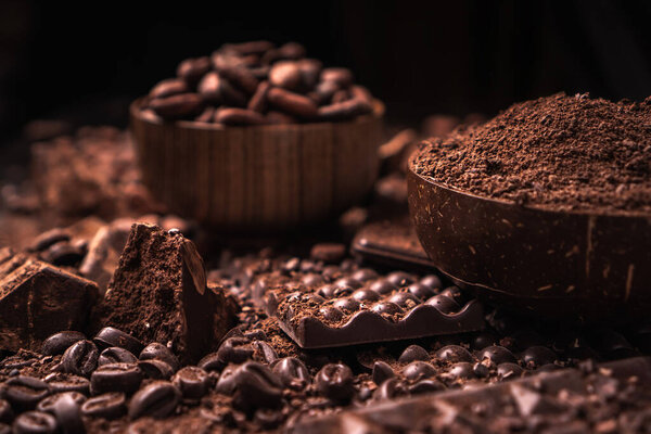 Какао-бобы, какао-порошок, масло какао, шоколадный батончик и шоколадный соус, шоколадный батончик в деревянной миске на темном фоне для текста
