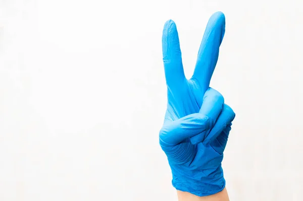 Eldivenli bir doktorun sol eli zafer işareti yapıyor. İyileştirme kavramı.