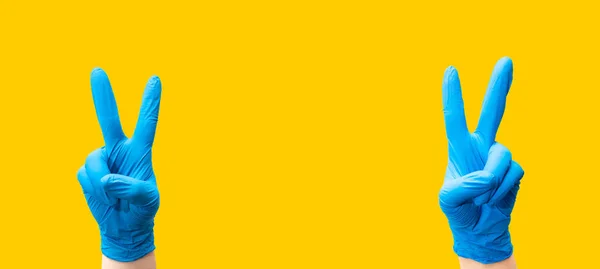 Koruyucu mavi eldivenli bir hemşirenin elleri zafer işareti yapıyor. İyileşme konsepti, dayak, koronavirüsü yenme.