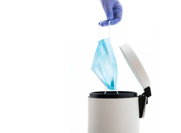 Eldivenli bir el, koruyucu yüz maskesini çöp kutusuna atıyor. Coronavirüs kavramının sonu. Covid-19 tedavisi gördü ve karantina sona erdi. Beyaz arkaplan.