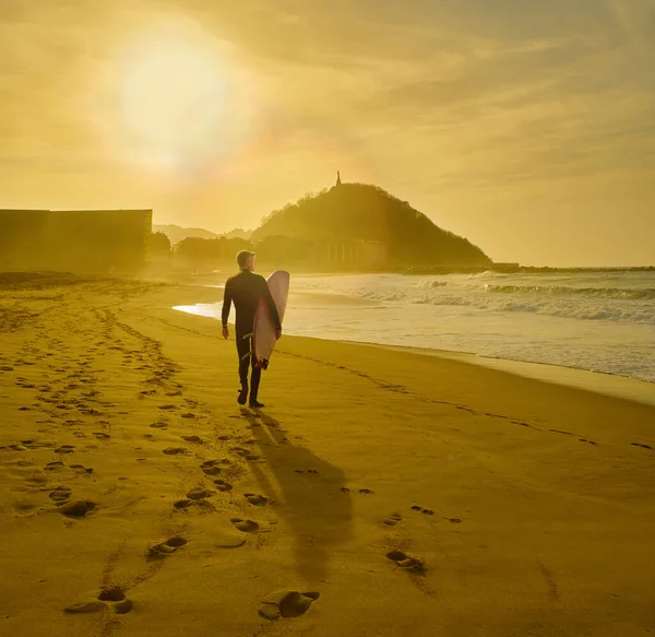 背景にモンテ ウルグルと夕日でチューリッヒビーチを歩くサーファー サンセバスティアン バスク地方 ギプスコア スペイン — ストック写真