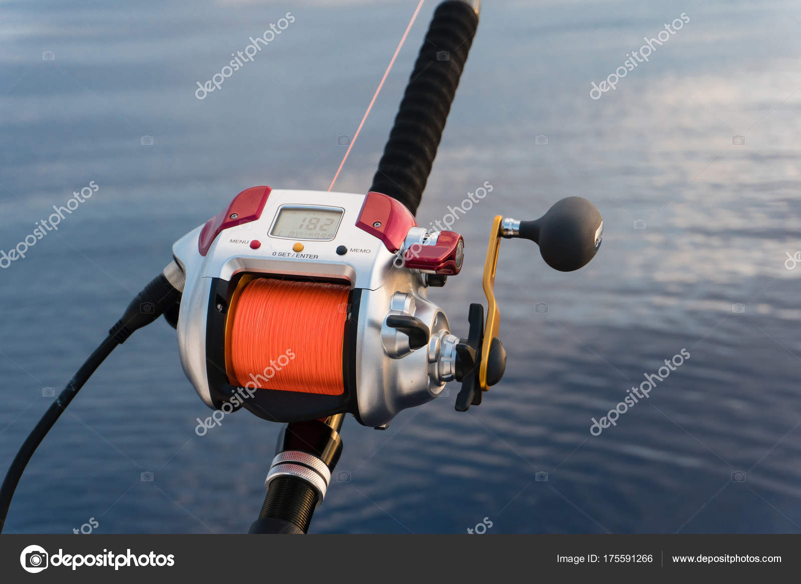 Electric fishing reel mounted on a rod with sea in the backgroun