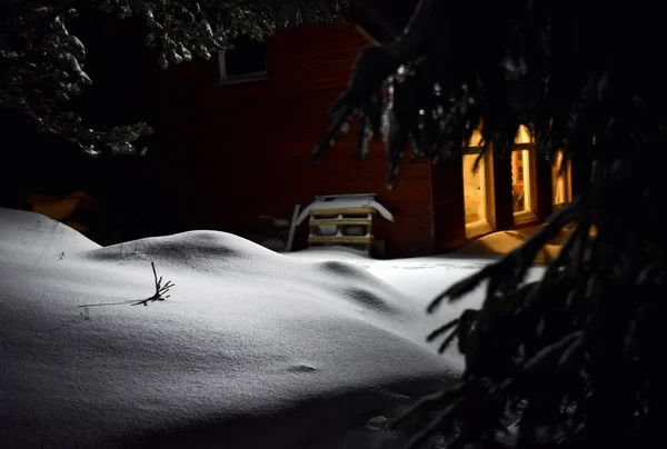Chimenea de luz de una casa de campo iluminar la nieve exterior en invierno —  Fotos de Stock
