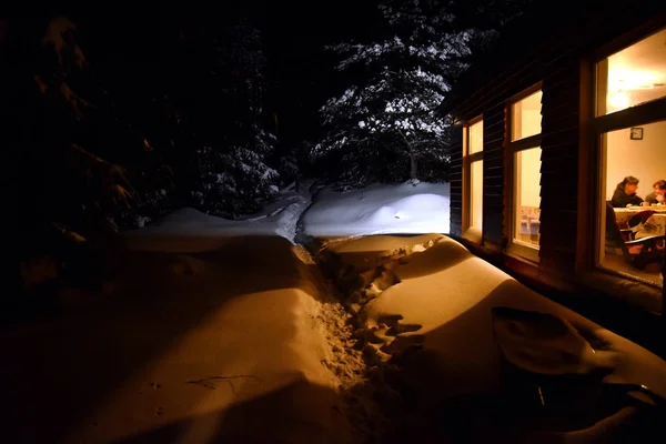 A luz de chaminé de uma casa de campo ilumina a neve fora no inverno — Fotografia de Stock