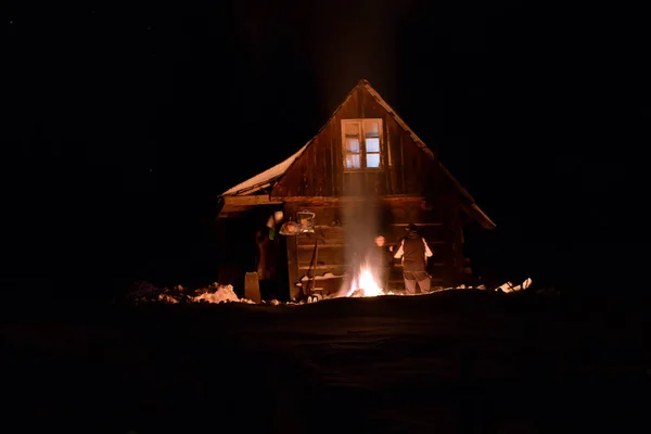 Turista aquecido pelo fogo no inverno perto de uma cabana de madeira — Fotografia de Stock