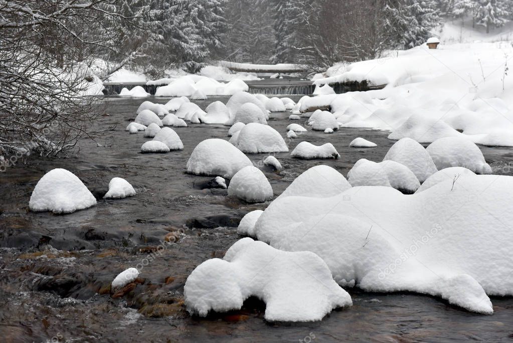 Small frozen river with fresh snow on the rocks