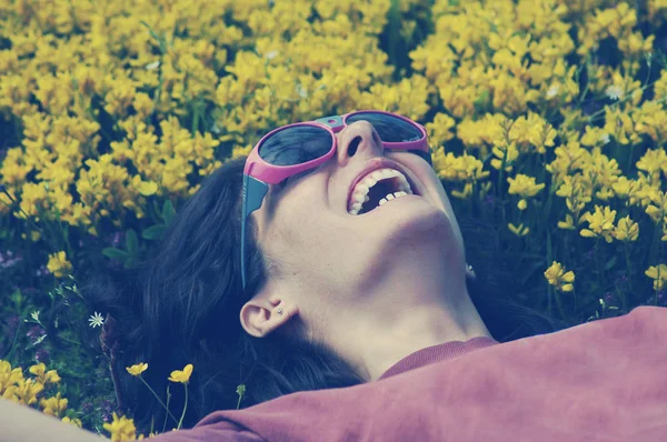 Mujer sonriente con gafas de sol acostada en un prado lleno de yello — Foto de Stock