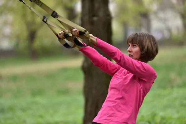 Kobieta robi broni, którą biceps curl szkolenie trx fitness paski — Zdjęcie stockowe