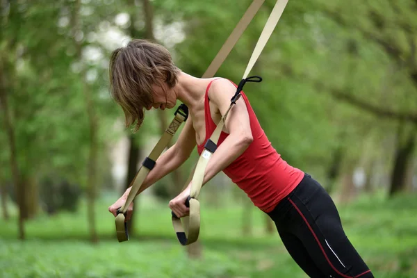 Mujer joven hace entrenamiento de suspensión con correas de fitness en el —  Fotos de Stock