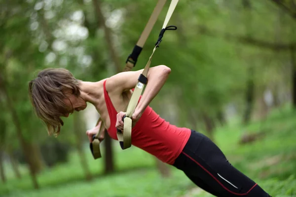 Young woman does suspension training with fitness straps in the — Stock Photo, Image