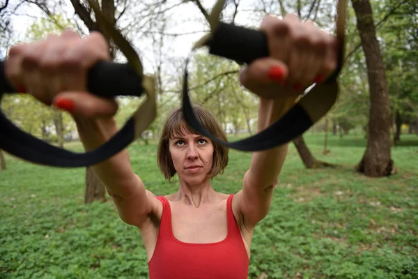 Γυναίκα κάνει όπλα μπούκλα δικέφαλων μυών κατάρτισης με ιμάντες trx γυμναστήριο — Φωτογραφία Αρχείου