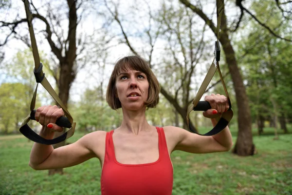 Kvinnan gör armar biceps curl träning med trx fitness remmar — Stockfoto