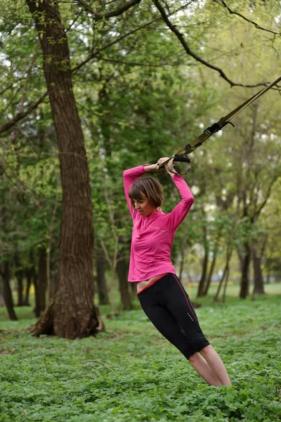 Jonge aantrekkelijke vrouw houdt lichaam uitrekken met trx fitness str — Stockfoto