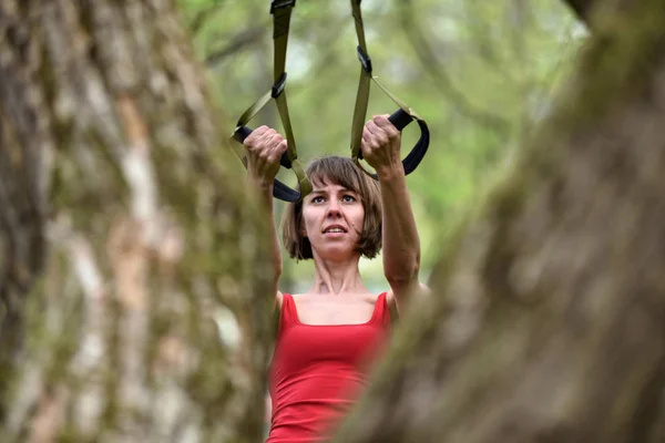 Γυναίκα κάνει όπλα μπούκλα δικέφαλων μυών κατάρτισης με ιμάντες trx γυμναστήριο — Φωτογραφία Αρχείου