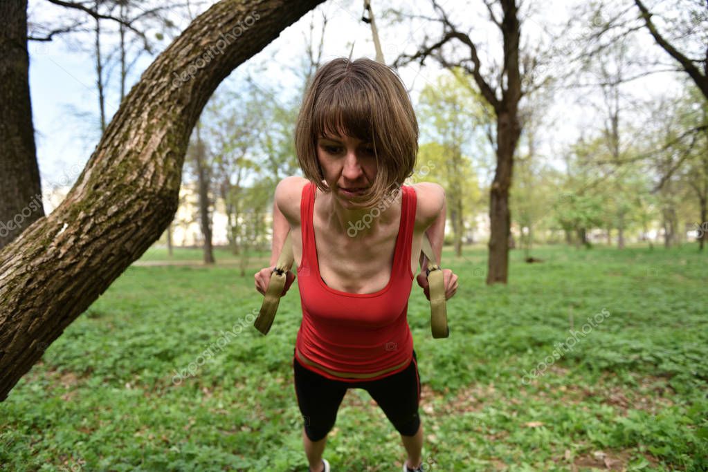 Young woman does suspension training with fitness straps in the 