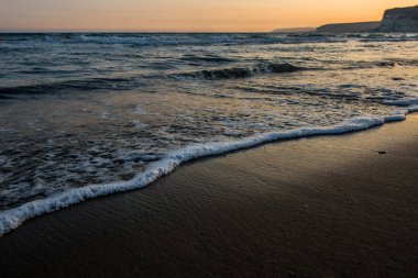 Gün batımı sırasında kumsala yaklaşırken dalgalar