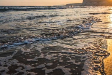 Gün batımı sırasında kumsala yaklaşırken dalgalar
