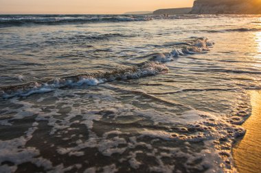 Gün batımı sırasında kumsala yaklaşırken dalgalar