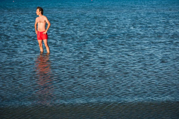 瘦瘦的小伙子在海水中的红色泳装摆姿势 — 图库照片