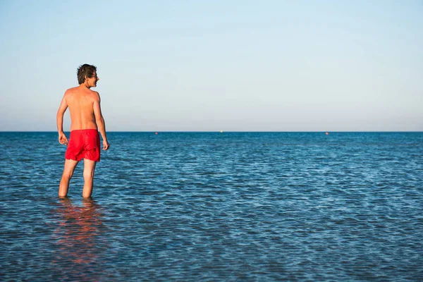 Slim guy posing in red swimwear in sea water