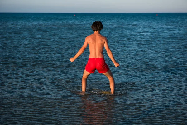 Slim guy posing in red swimwear in sea water — Stock Photo, Image