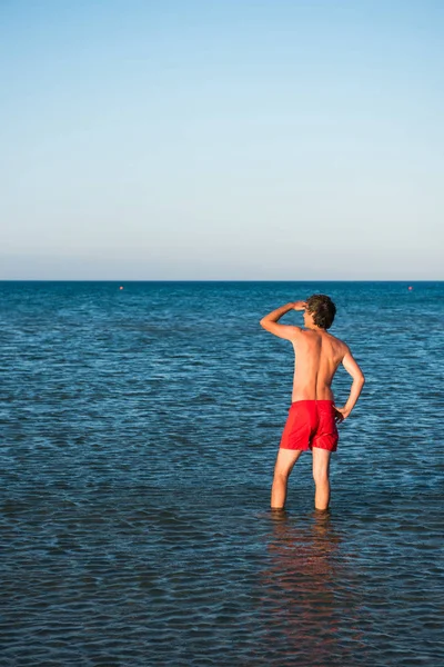 Slim guy posing in red swimwear in sea water — Stock Photo, Image