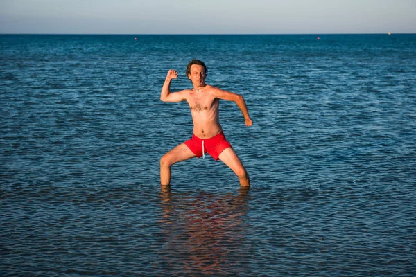 海の水で赤い水着でポーズをとってスリムな男 — ストック写真