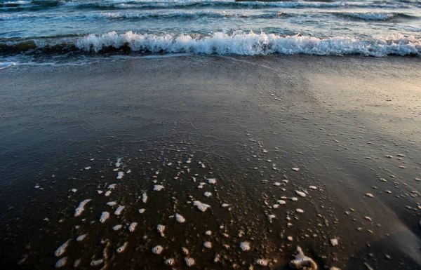 Волны приближаются к песчаному пляжу на закате — стоковое фото