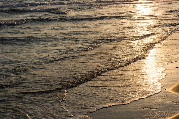 Волны приближаются к песчаному пляжу на закате — стоковое фото