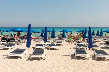 Tourists relaxing on sunbeds on a sandy beach under beach umbrel clipart