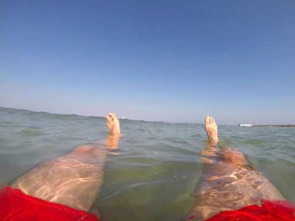 Gambe di nuotatore in costume da bagno rosso galleggiante in mare — Foto Stock