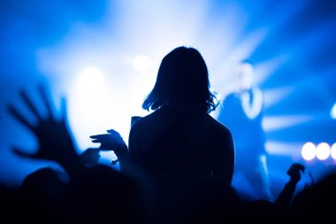 Parlak sahne ışıkları önünde konser kalabalığının silueti.