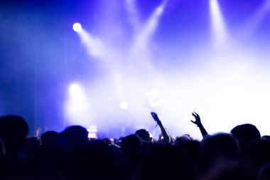 Parlak sahne ışıkları önünde konser kalabalığının silueti.