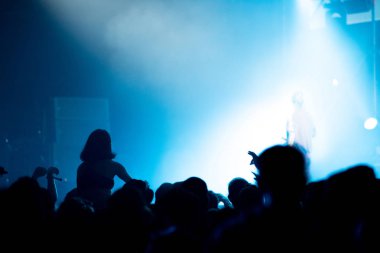 Parlak sahne ışıkları önünde konser kalabalığının silueti.