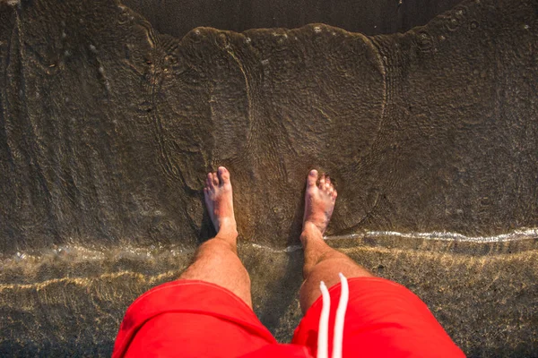 I piedi dell'uomo nella sabbia, onde che si avvicinano alla spiaggia — Foto Stock