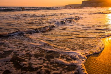 Gün batımı sırasında kumsala yaklaşırken dalgalar