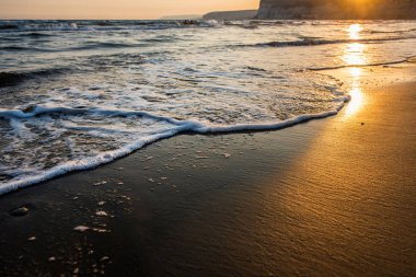 Gün batımı sırasında kumsala yaklaşırken dalgalar