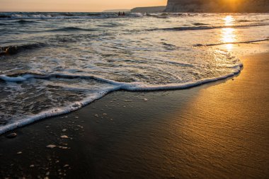 Gün batımı sırasında kumsala yaklaşırken dalgalar