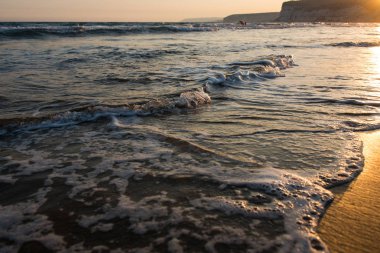 Gün batımı sırasında kumsala yaklaşırken dalgalar