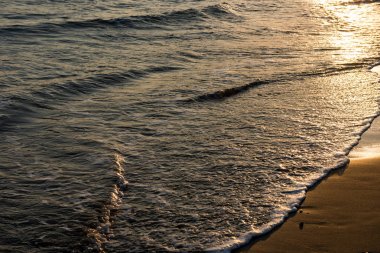 Gün batımı sırasında kumsala yaklaşırken dalgalar
